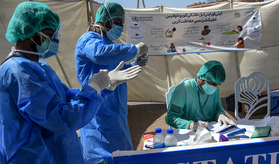 Medical staff members wearing protective gear work on a desk at a drive-through screening and testing facility point during a government-imposed nationwide lockdown as a preventive measure against the COVID-19 coronavirus, at the port city of Karachi on April 4, 2020. (AFP/ File)