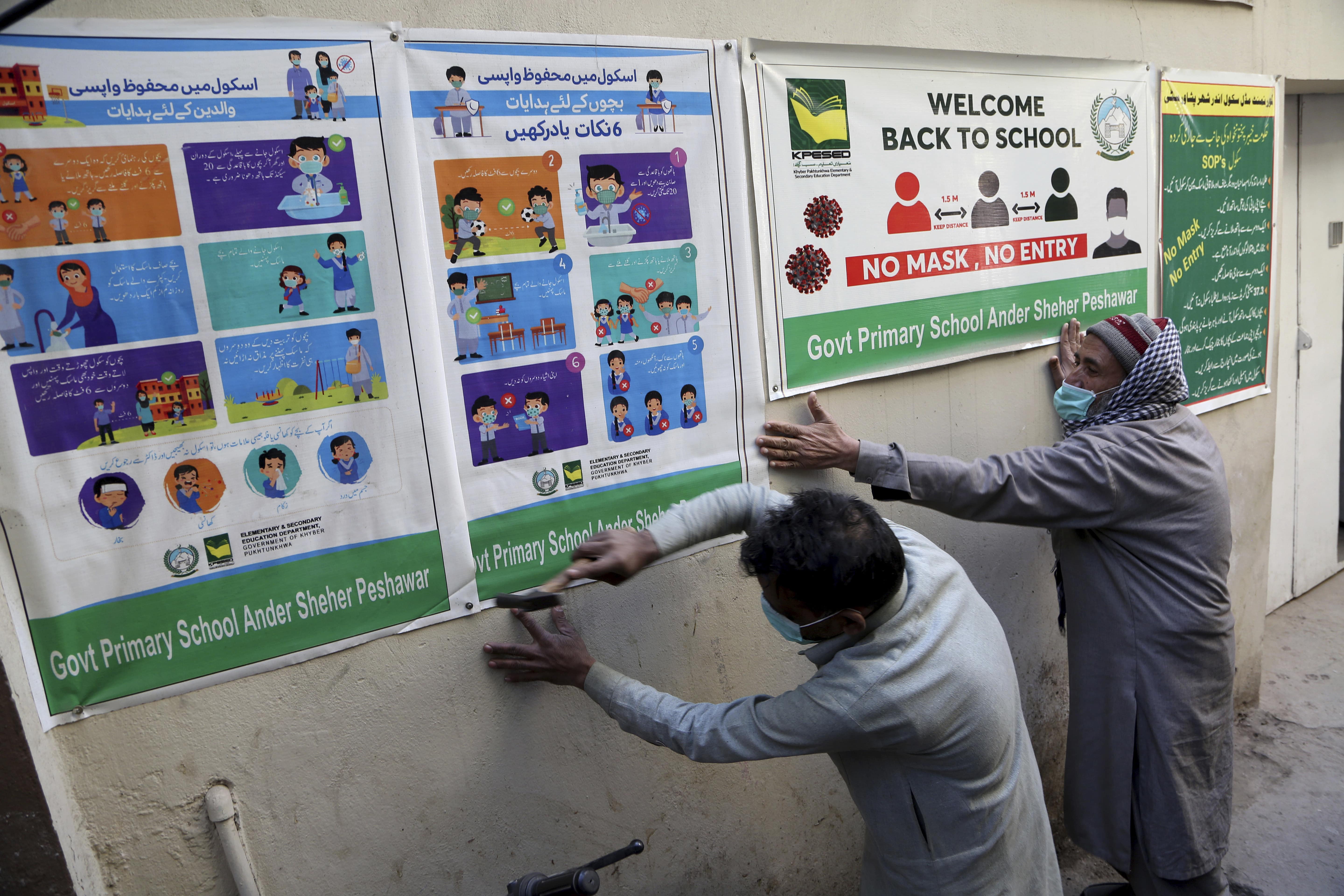 Workers fix posters informing of precautions to help prevent the spread of COVID-19 on the outer wall of a school, in Peshawar, Pakistan, Saturday, Jan. 30, 2021. Pakistani authorities will reopen middle schools on Feb. 1. (AP)