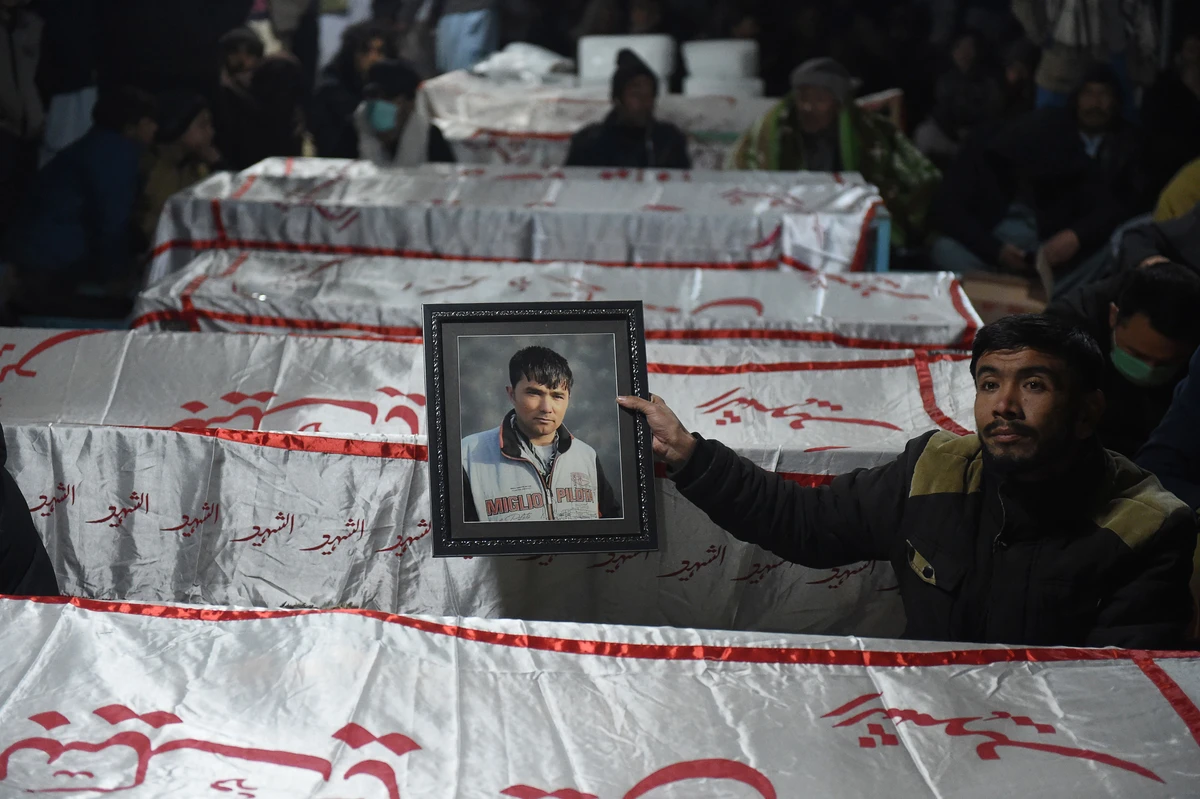 A mourner from a Shiite Hazara community holds a photograph of a victim near the coffins of other miners who were killed in an attack by gunmen in the mountainous Machh area, on the outskirts of Quetta on January 4, 2021. (AFP)