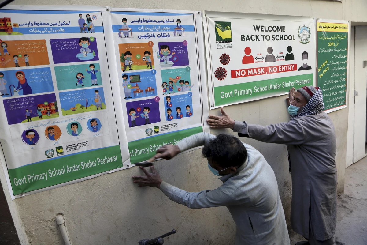 Workers fix posters informing of precautions to help prevent the spread of COVID-19 on the outer wall of a school, in Peshawar, Pakistan, Saturday, Jan. 30, 2021. Pakistani authorities will reopen middle schools on Feb. 1. (AP)