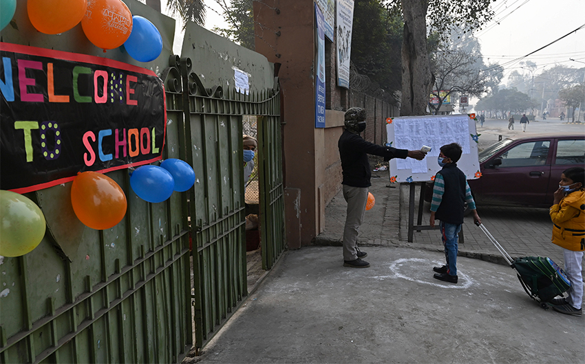 A staff member checks the body temperature of a student upon his arrival at a school in Lahore on February 1, 2021. (AFP)