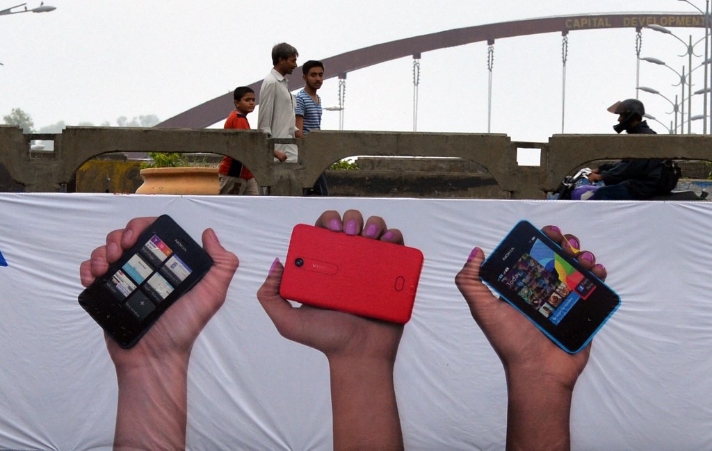Pakistani pedestrians walk past a mobile phone promotion banner in Islamabad on August 6, 2013. (AFP/File)