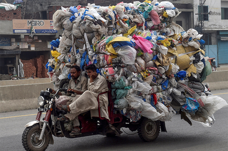 In this picture taken on July 31, 2019, men drive a three-wheeler loaded with used plastic bags in Lahore, Pakistan. (AFP/File)