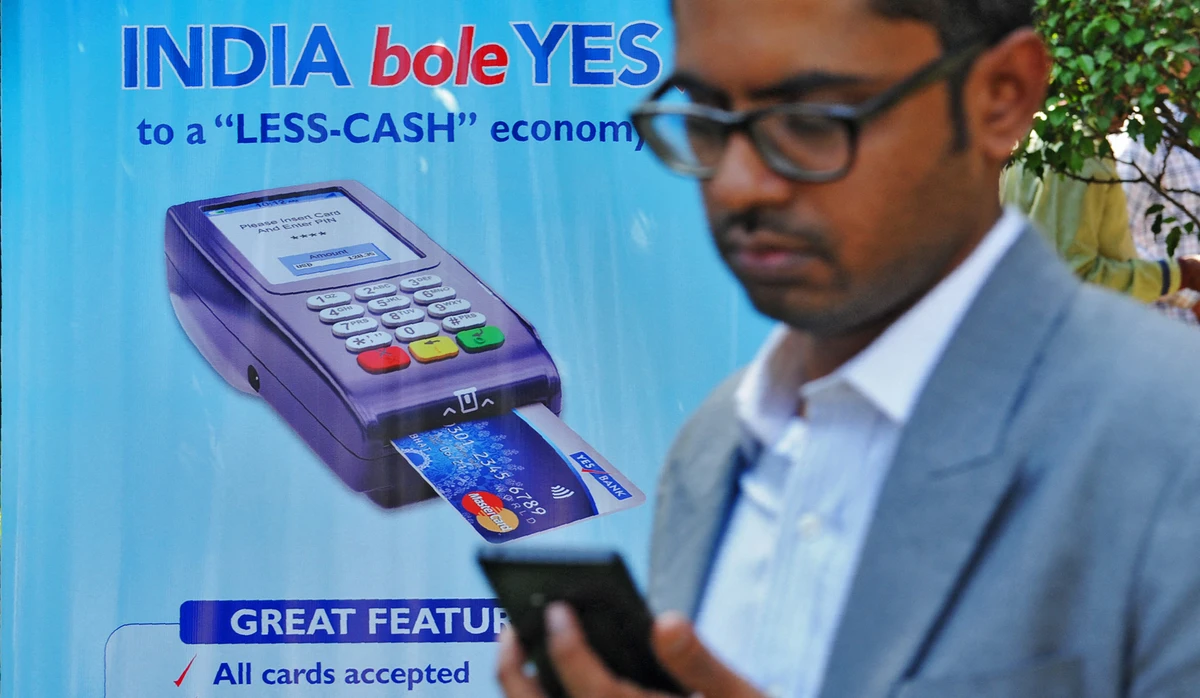 An Indian bank teller checks his phone as he walks past a poster advertising electronic payments at a Digital Wealth Fair in Mumbai, India on January 3, 2017. (AFP/File)