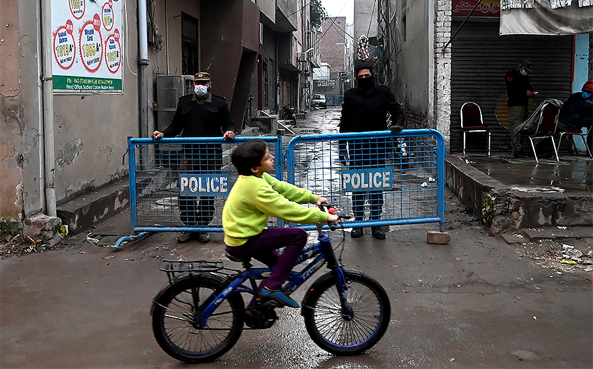 A boy cycles past policemen standing on guard in a cordon off street after authorities sealed the residential area as Covid-19 cases continue to rise in Lahore, Pakistan, on December 9, 2020. (AFP/File)