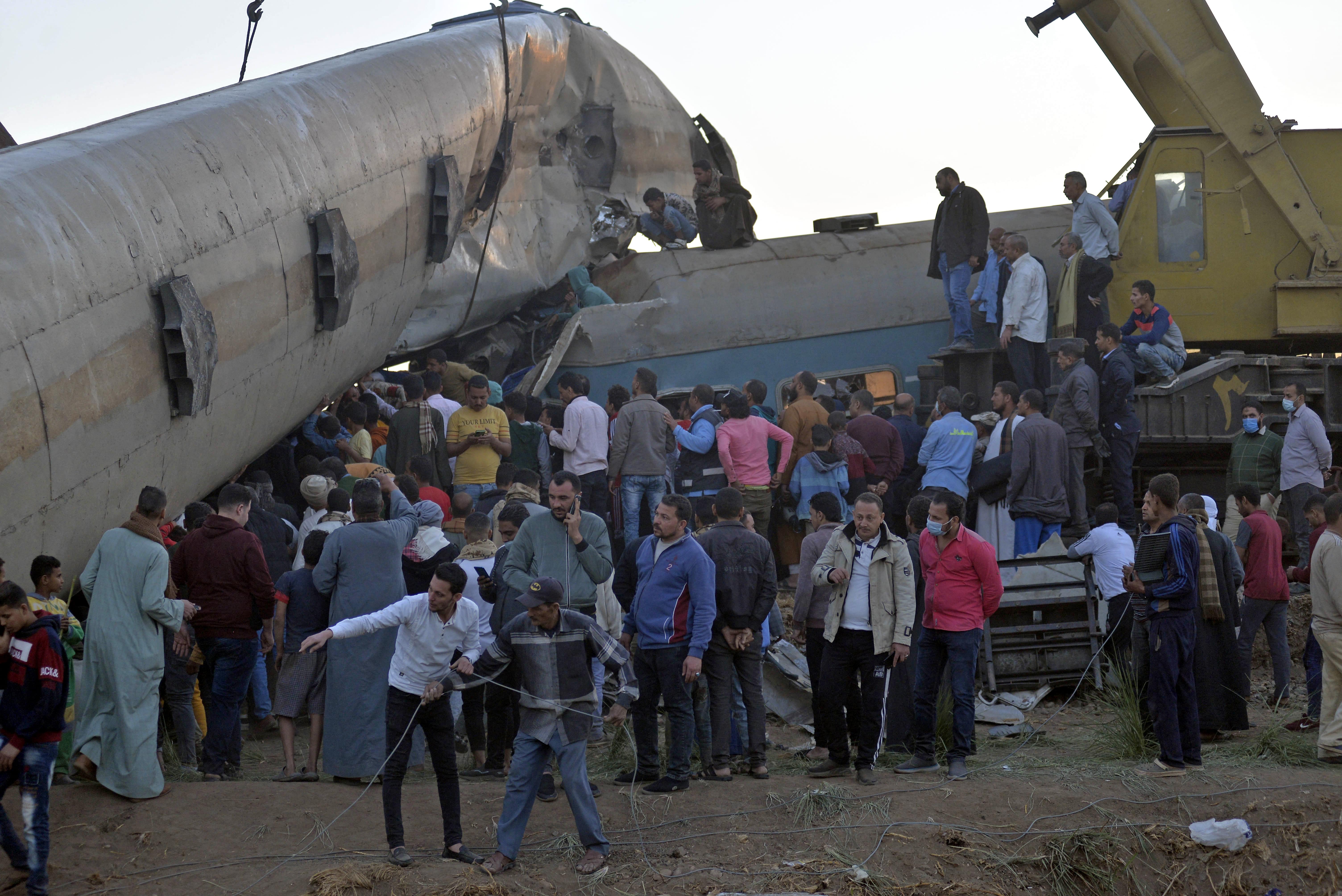People gather around the wreckage of two trains that collided in the Tahta district of Sohag province, some 460 kilometres (285 miles) south of the Egyptian capital Cairo, reportedly killing at least 32 people and injuring scores of others, on March 26, 2021. (AFP)