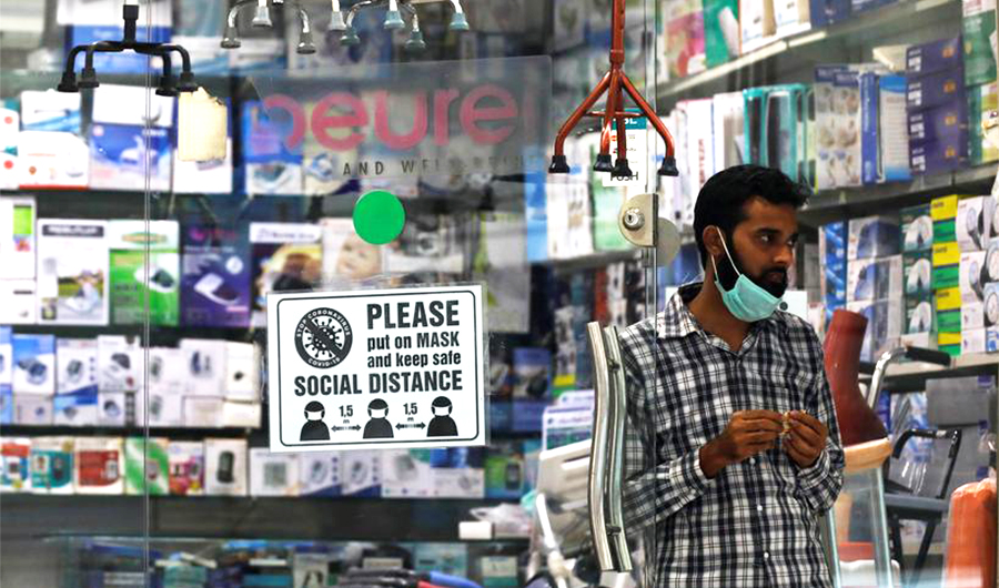 A man with a mask on his chin stands at the entrance of his shop for medical and fitness supplies displaying a precautionary sign for the customers as the outbreak of the coronavirus disease continues, in Karachi, Pakistan December 8, 2020. (REUTERS)