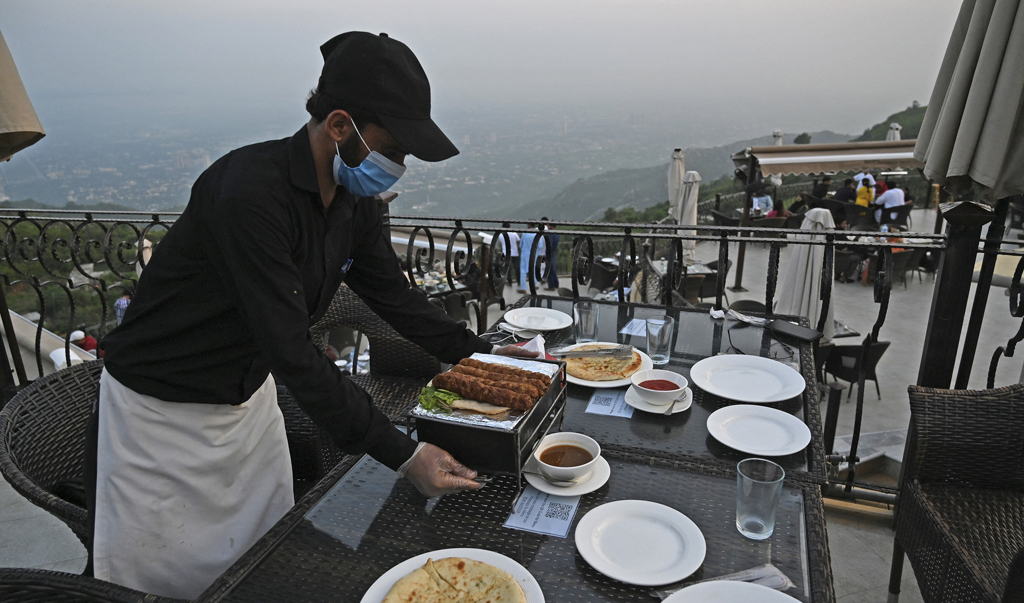 A waiter serves food on a table at a rooftop restaurant on Margalla Hills in Islamabad, Pakistan, on August 10, 2020. (AFP/File)