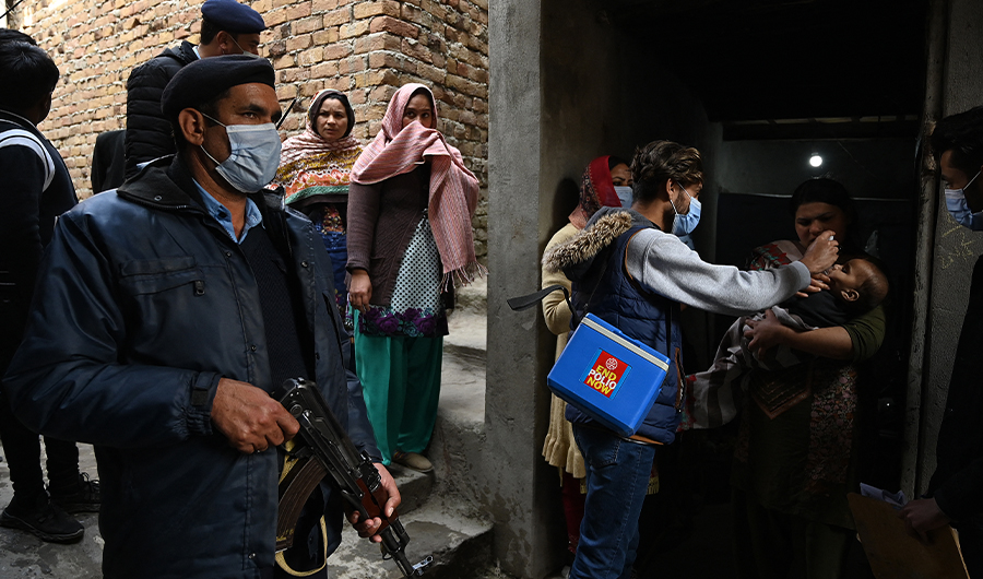 A policeman (L) stands guard as a health worker administers polio vaccine drops to a child during a polio vaccination door-to-door campaign in a slum area in Islamabad on January 13, 2021. (AFP)