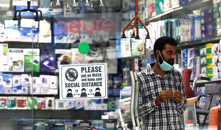 A man with a mask on his chin stands at the entrance of his shop for medical and fitness supplies displaying a precautionary sign for the customers as the outbreak of the coronavirus disease continues, in Karachi, Pakistan December 8, 2020. (REUTERS)