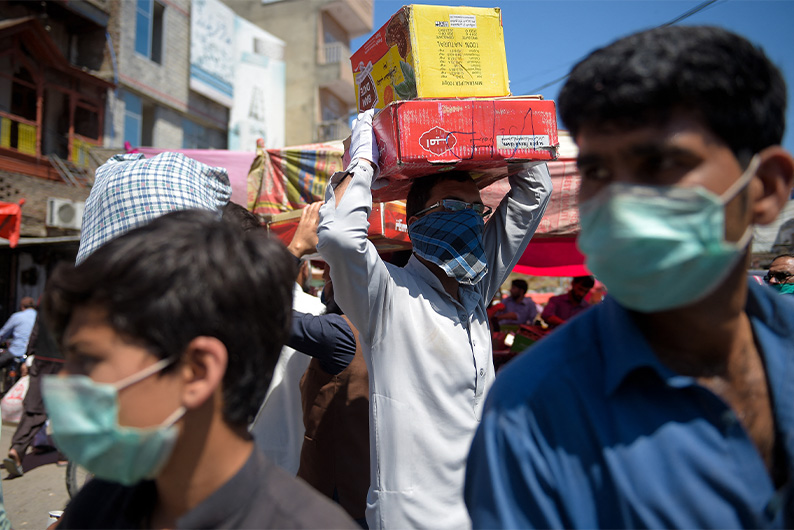 A labourer (center) carries boxes of dates at a market in Rawalpindi on April 19, 2020. (AFP)
