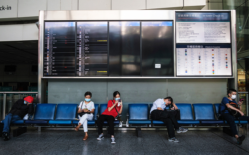 People wear face masks as they sit under a flight departure board at the currently closed in-town check-in for Hong Kong's international airport on July 16, 2020. (AFP/File)