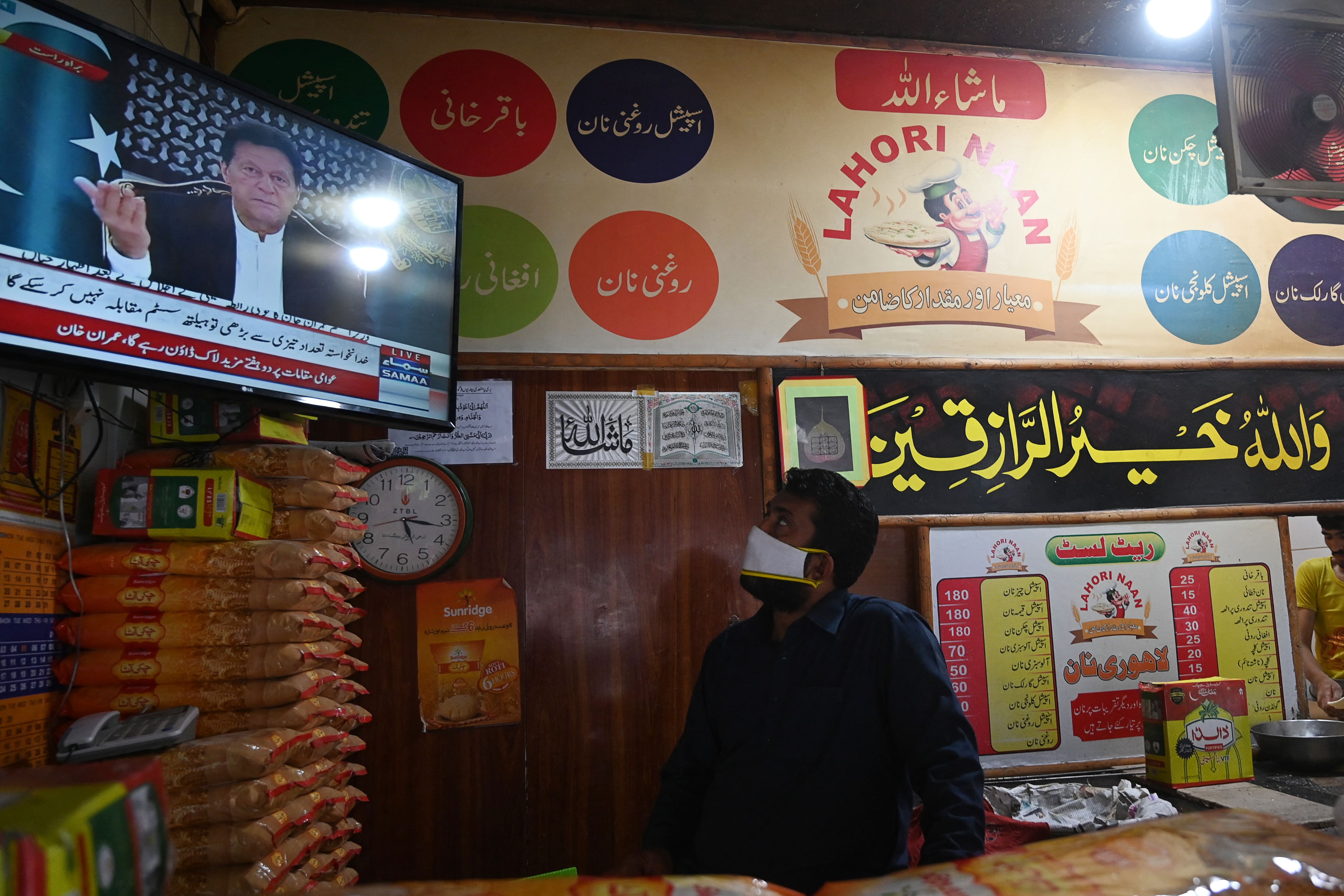 A bread maker wearing a facemask watches on television Pakistan's Prime Minister Imran Khan (L top) addressing the nation, Islamabad, April 14, 2020. (AFP /File photo)