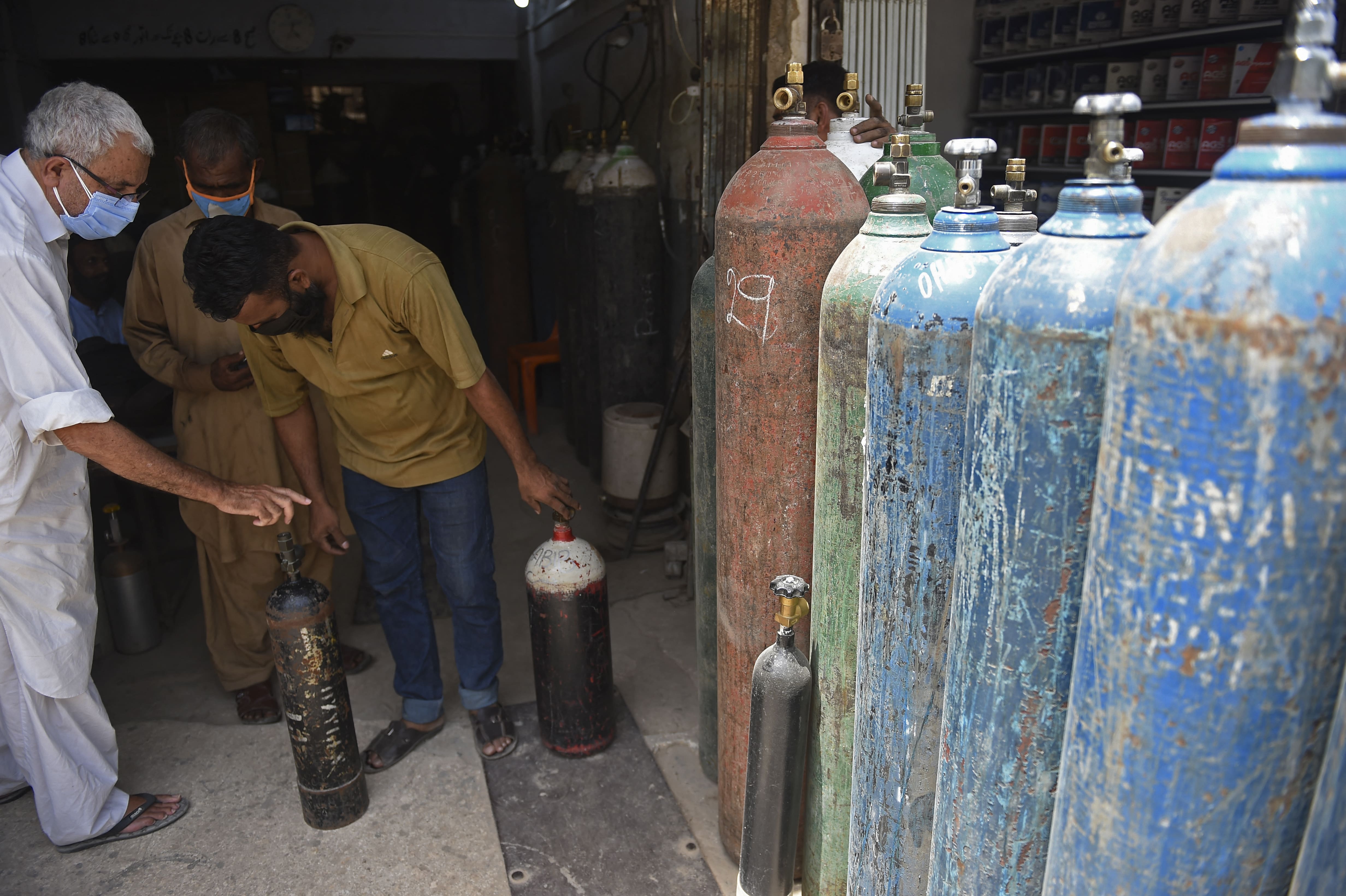 A shopkeeper (R) deals with a customer before refilling medical oxygen cylinders for Covid-19 coronavirus patients at his shop in Karachi on April 26, 2021. (AFP)
