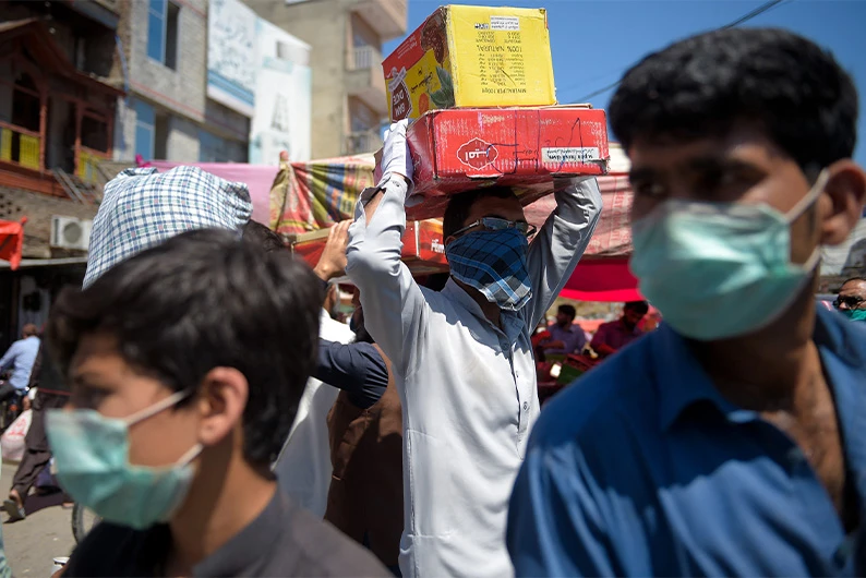 A labourer (center) carries boxes of dates at a market in Rawalpindi on April 19, 2020. (AFP)