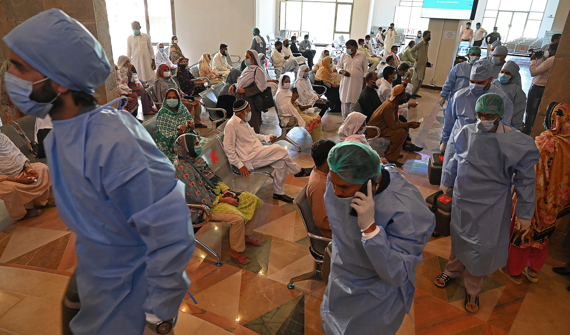 Health workers carrying vaccine carriers arrive as people wait for their turn to get inoculated with the jab of CanSino Biologics' Covid-19 coronavirus vaccine at a vaccination camp held in Islamabad, Pakistan, on May 19, 2021. (AFP)