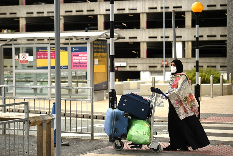 A passenger wearing PPE (personal protective equipment), including a face mask as a precautionary measure against COVID-19, pushes his luggage after at Manchester Airport in northern England, on June 8, 2020. (AFP)