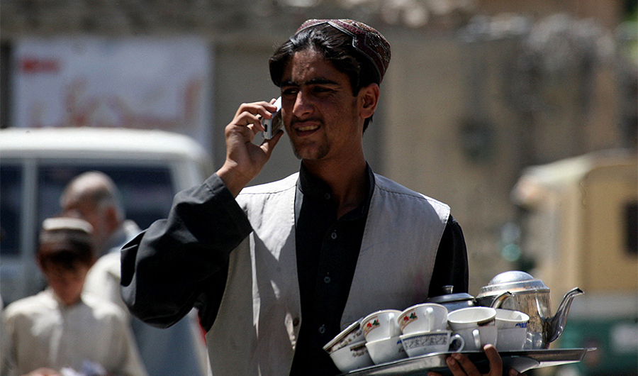 A Pakistani tea seller carries a tray with cups of tea while he talks on a mobile phone at a street in Quetta on May 11, 2010. (AFP)