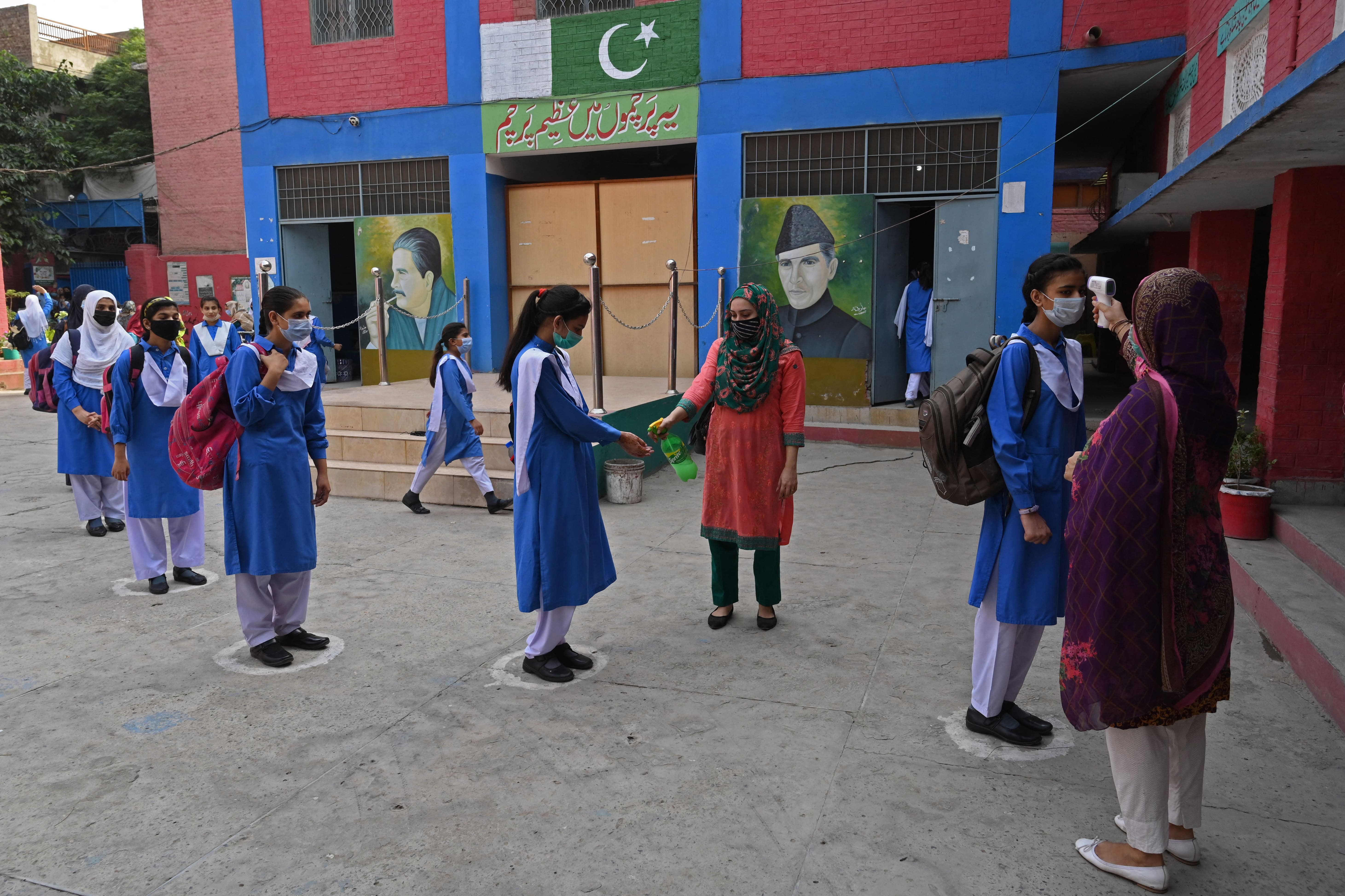 A staff member checks the body temperature of students upon their arrival at a school in Lahore on June 7, 2021, as the government reopened educational institutes after remaining closed as a preventive measure amid Covid-19 coronavirus pandemic. (AFP)