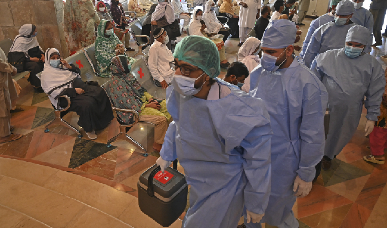 Health workers carrying vaccine carriers arrive as people wait for their turn to get inoculated with the coronavirus vaccine at a vaccination camp held in Islamabad, Pakistan, on May 19, 2021. (AFP/File)