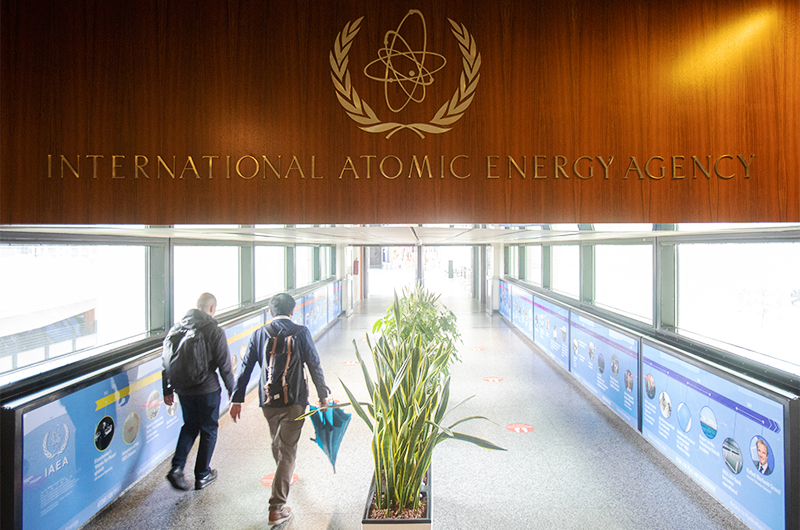 People walk under the sign of the International Atomic Energy Agency at the IAEA headquarters in Vienna on May 23, 2021. (AFP/File)