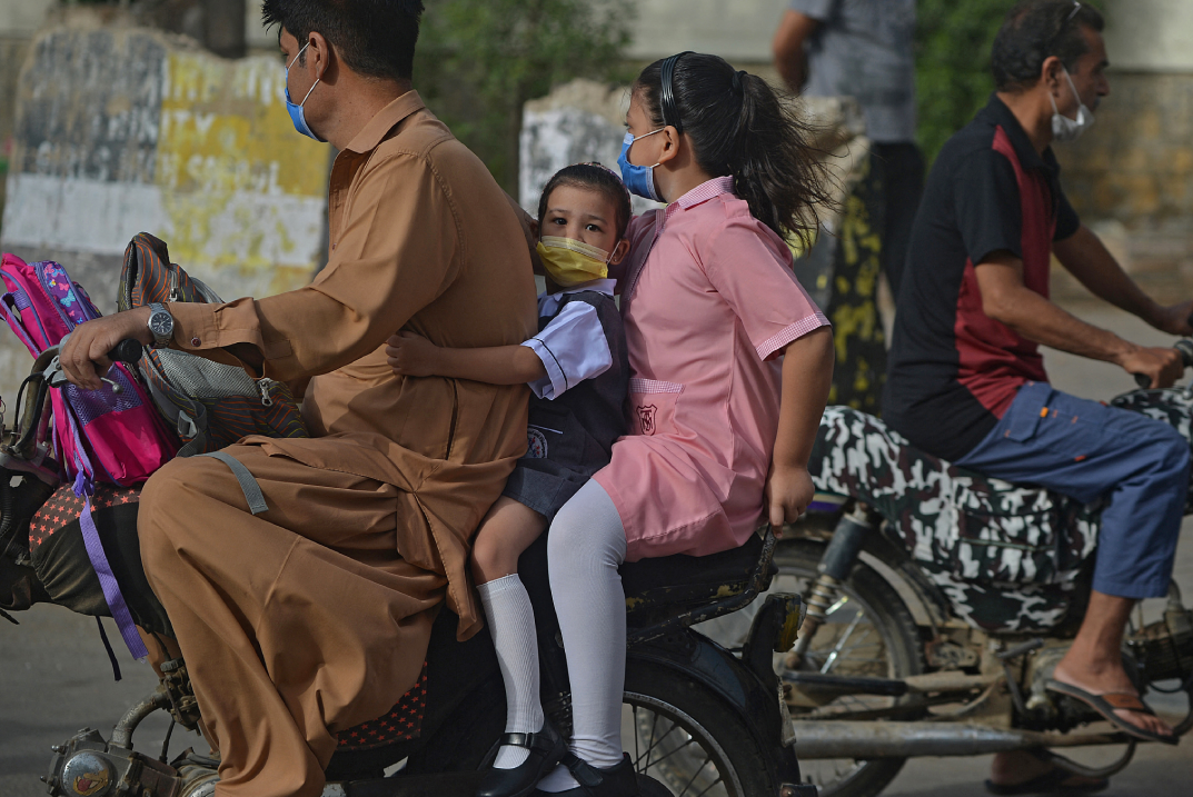 Children riding as a pillion on a motorcycle on their way to a school in Karachi on June 21. (AFP)