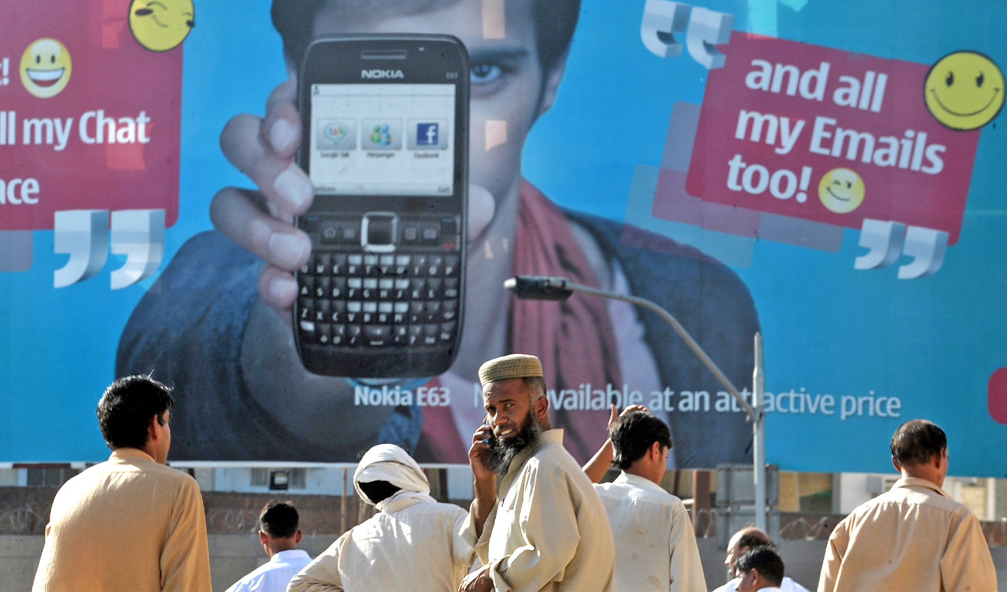 Pakistani pedestrians wait for transport as they stand in front of an advertisement for a cellular telephone in Rawalpindi on May 14, 2010. (AFP/File)
