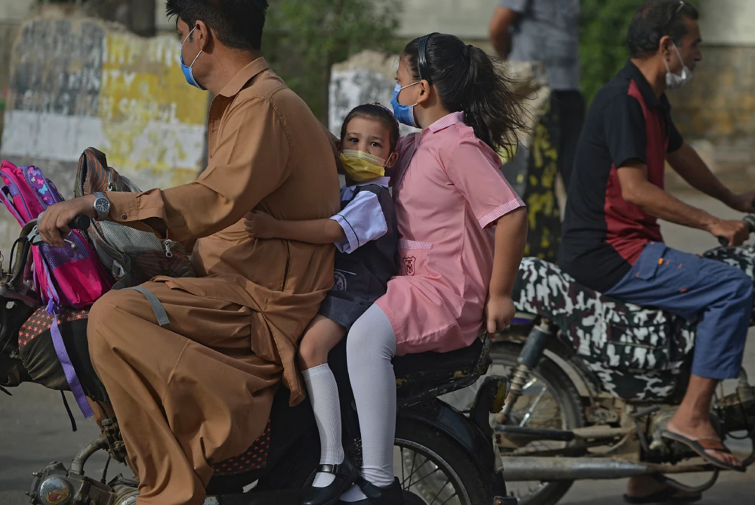 Children riding as a pillion on a motorcycle on their way to a school in Karachi on June 21. (AFP)