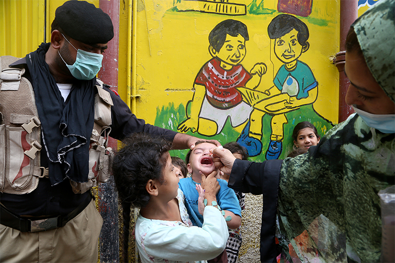 A police officer helps a health worker administer a polio vaccine to a child in Peshawar, Pakistan, Friday, July 30, 2021. (AFP)