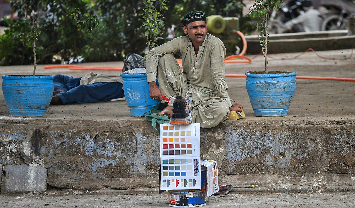 Daily wage labourers sit along a road waiting for customers to hire them for a day job in Karachi, Pakistan, on July 25, 2021. (AFP)