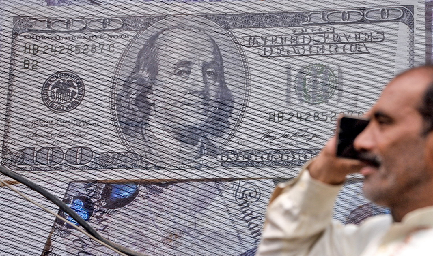 A Pakistani man talks on the phone in front of a poster displaying US dollars at the currency exchange place in Lahore, Pakistan, on May 16, 2019. (AFP/File)
