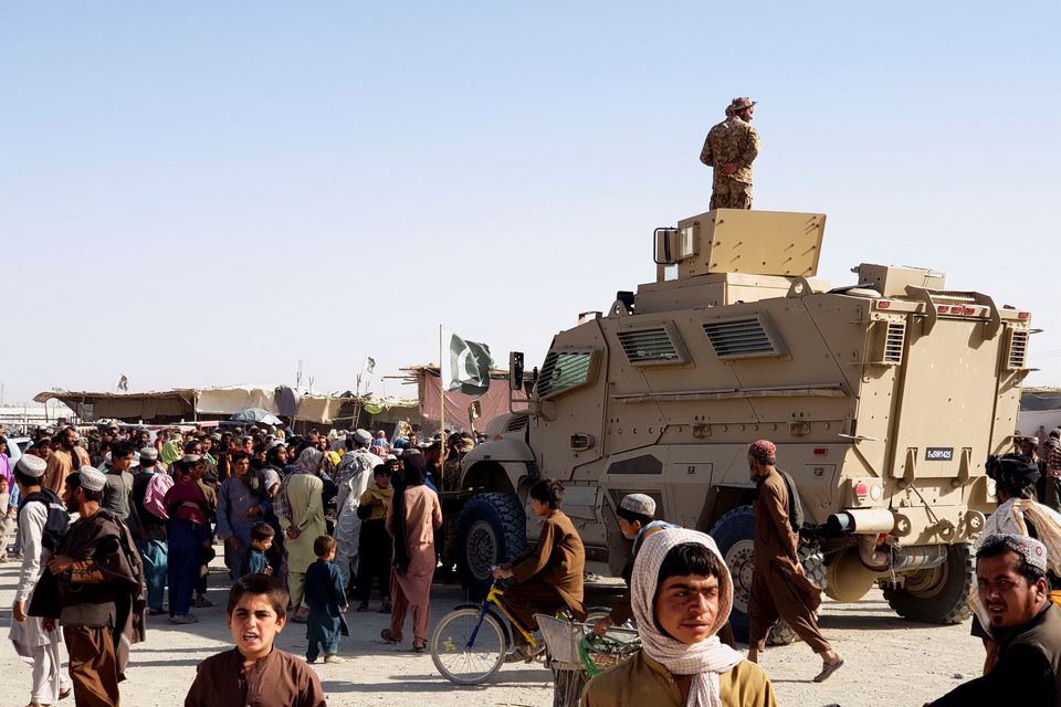 A Pakistan's Army soldier stands guard on a vehicle as people gather and wait to cross at the Friendship Gate crossing point in the Pakistan-Afghanistan border town of Chaman, Pakistan August 12, 2021. (REUTERS)
