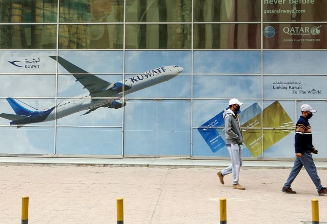 Men, wearing protective masks, walk past a billboard for Kuwait airways in Kuwait City on March 14, 2020. (AFP/File)