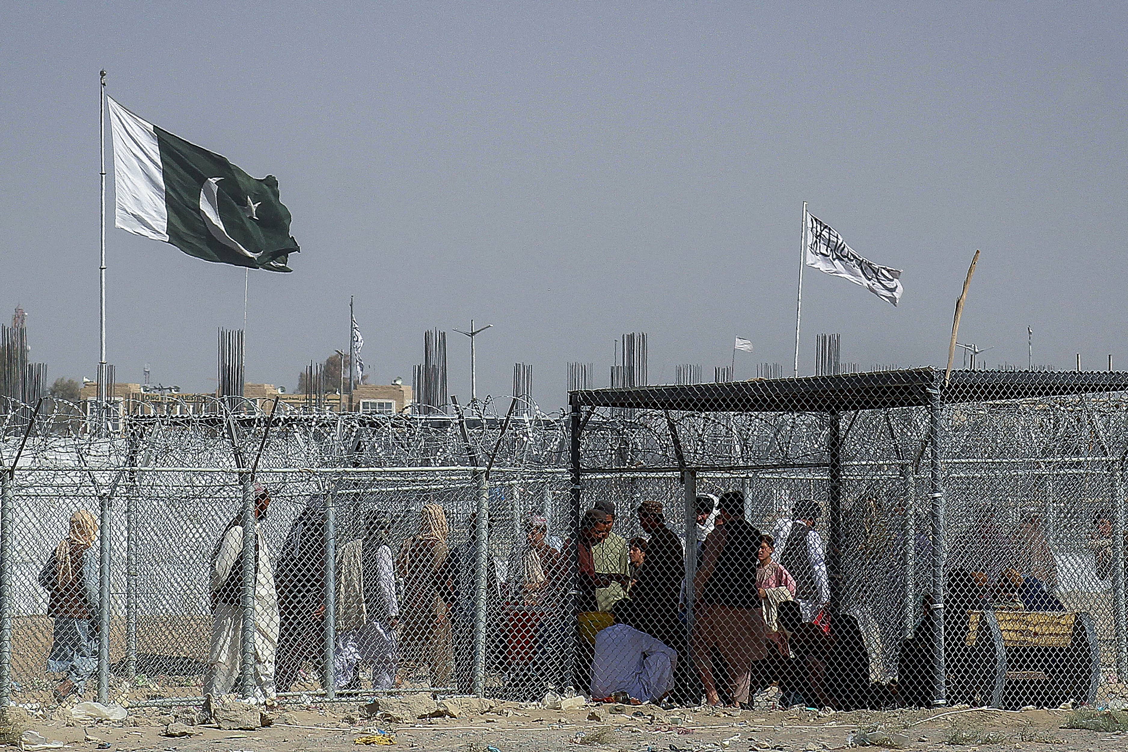 Afghan and Pakistani nationals walk through a security barrier to cross the border as a national flag of Pakistan and a Taliban flag is masted in the Pakistan-Afghanistan border crossing point in Chaman on August 24, 2021, following Taliban's military takeover of Afghanistan. (AFP)