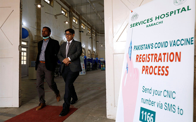 People walk past a sign outside the Khaliq Dina Hall and Library, which has been converted to be used as a vaccination centre, to administering coronavirus disease vaccine, in Karachi, Pakistan February 1, 2021. (REUTERS)