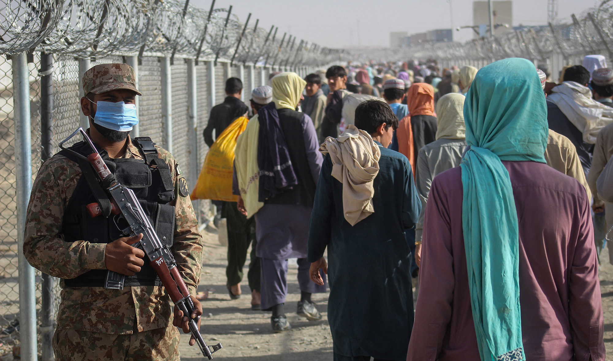 A Pakistani soldier stands guard as Afghans walk along fences after arriving in Pakistan through the Pakistan-Afghanistan border crossing point in Chaman on August 26, 2021. (AFP)