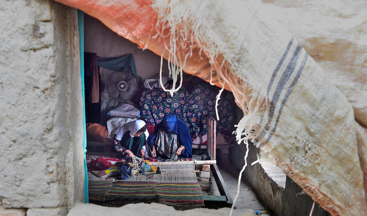 In this picture taken on February 12, 2020, Afghan refugee women make carpet at their home in a refugee camp in Peshawar. (AFP/File)
