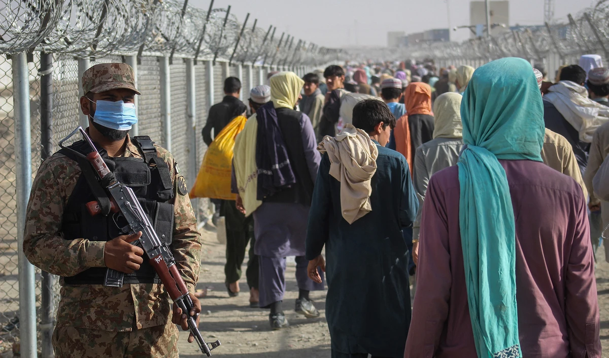 A Pakistani soldier stands guard as Afghans walk along fences after arriving in Pakistan through the Pakistan-Afghanistan border crossing point in Chaman on August 26, 2021. (AFP)