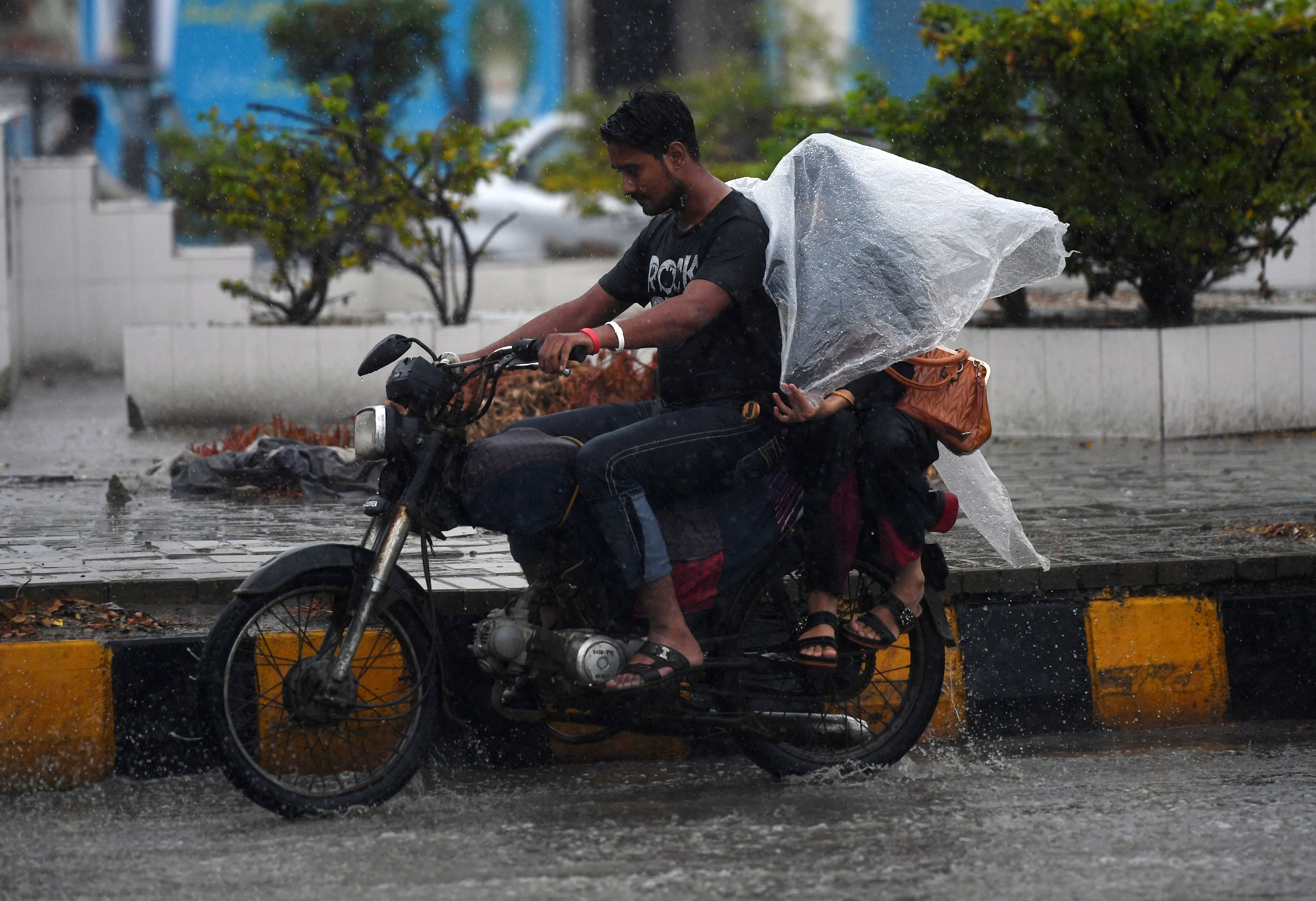 A Pakistani motorcyclist rides on a street as their passenger tries to keep dry under plastic covering during monsoon rain in Karachi on July 29, 2019. (AFP/ File)
