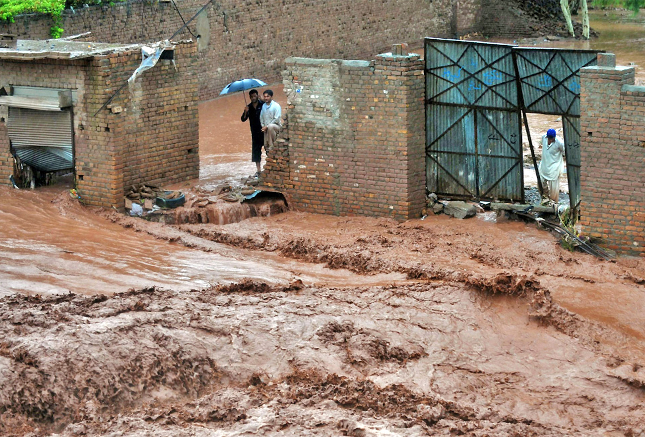 Residents watch water pour through a street on the outskirts of Peshawar, Pakistan, on July 28, 2010. (AFP/File)