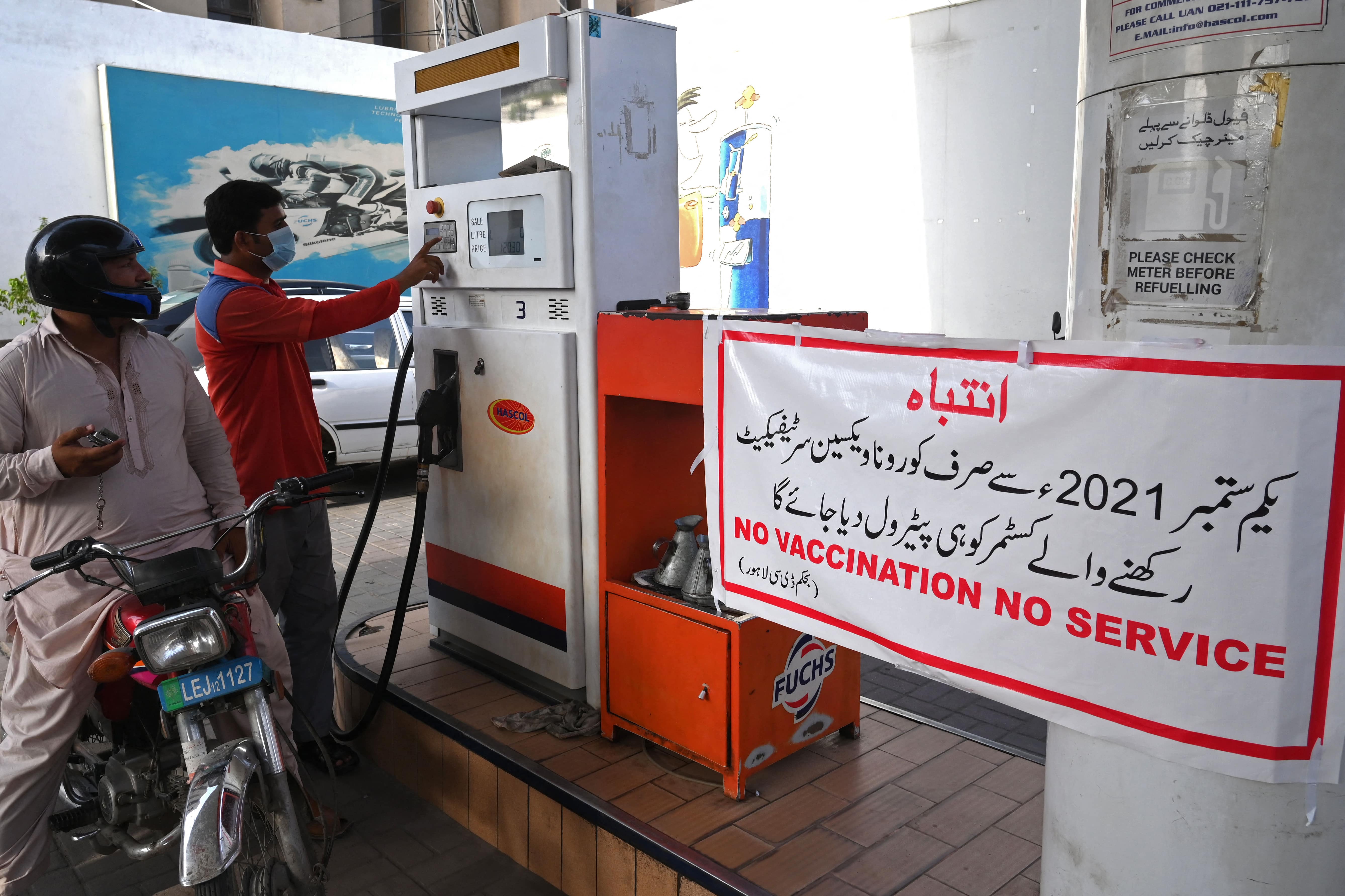 A worker prepares to fill the petrol tank of a motorbike next to a banner warning customers about the guidelines that from September onwards only Covid-19 coronavirus vaccinated customers will be allowed to purchase the fuel in Punjab province, in Lahore on August 27, 2021. (AFP)