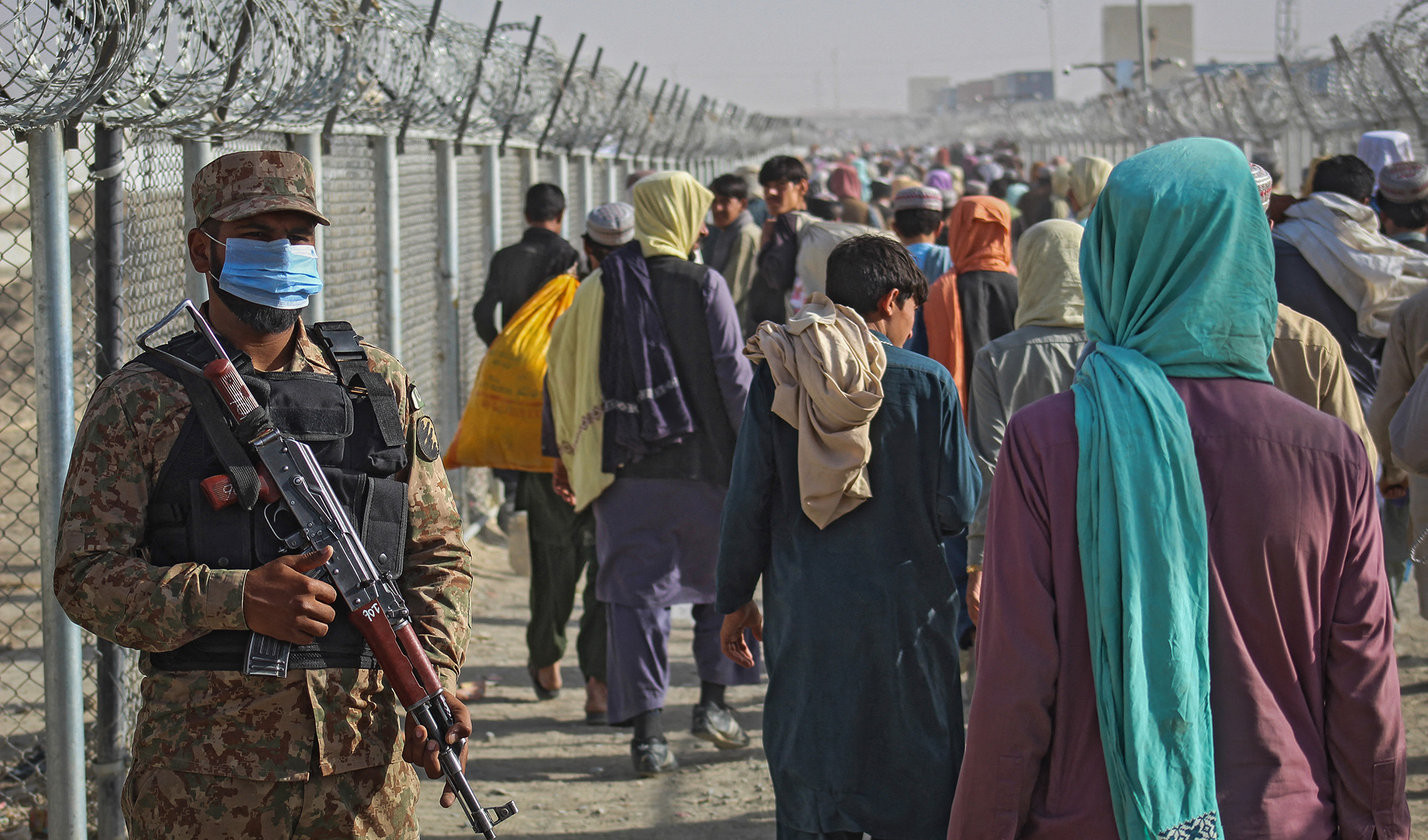 A Pakistani soldier stands guard as Afghans walk along fences after arriving in Pakistan through the Pakistan-Afghanistan border crossing point in Chaman on August 26, 2021. (AFP/File)