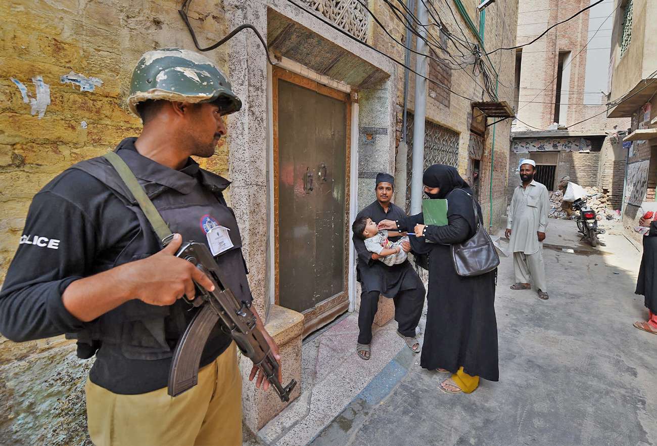 A Pakistani policeman stands guard as a health worker administers polio drops to a child during a polio vaccination campaign in Peshawar, Pakistan, on September 14, 2015. (AFP/File)