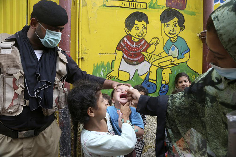 A police officer helps a health worker administer a polio vaccine to a child in Peshawar, Pakistan, Friday, July 30, 2021. (Photo courtesy: AP)