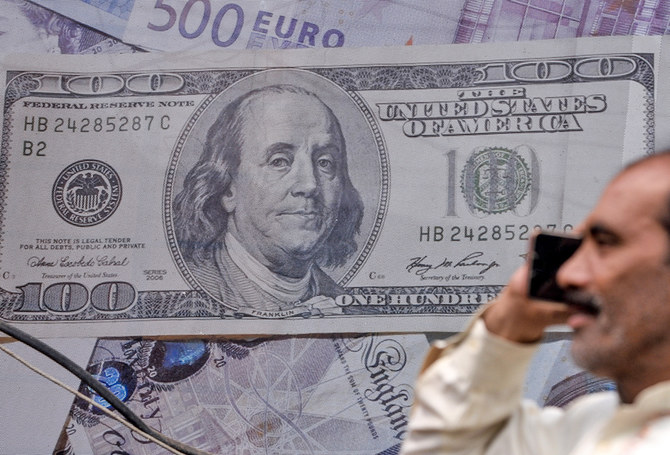 A Pakistani man talks on the phone in front of a poster displaying US dollars at the currency exchange place in Lahore, Pakistan, on May 16, 2019. (AFP/File)