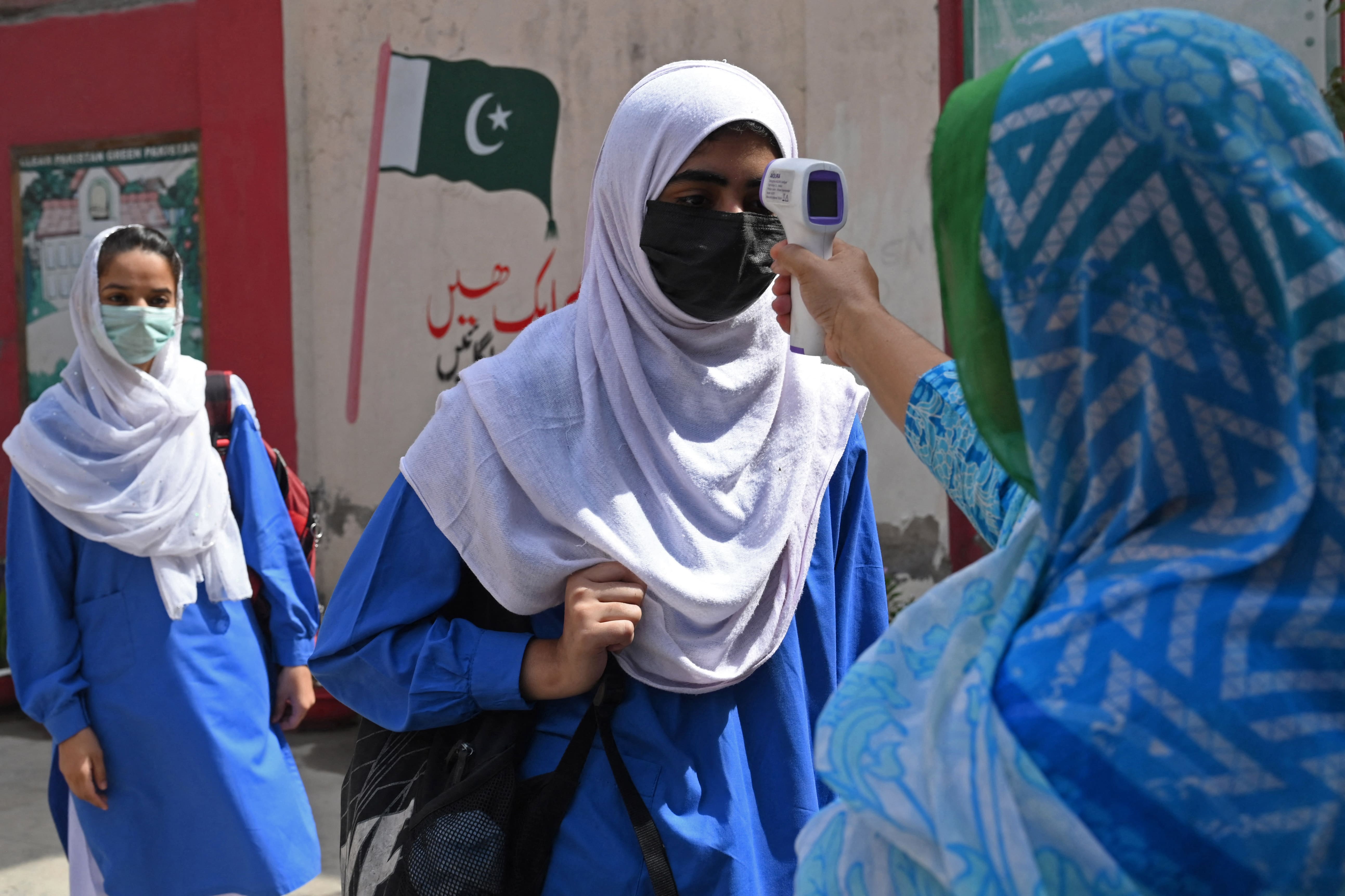 A teacher checks the body temperature of a student upon her arrival at a school in Lahore on May 31, 2021. (AFP)