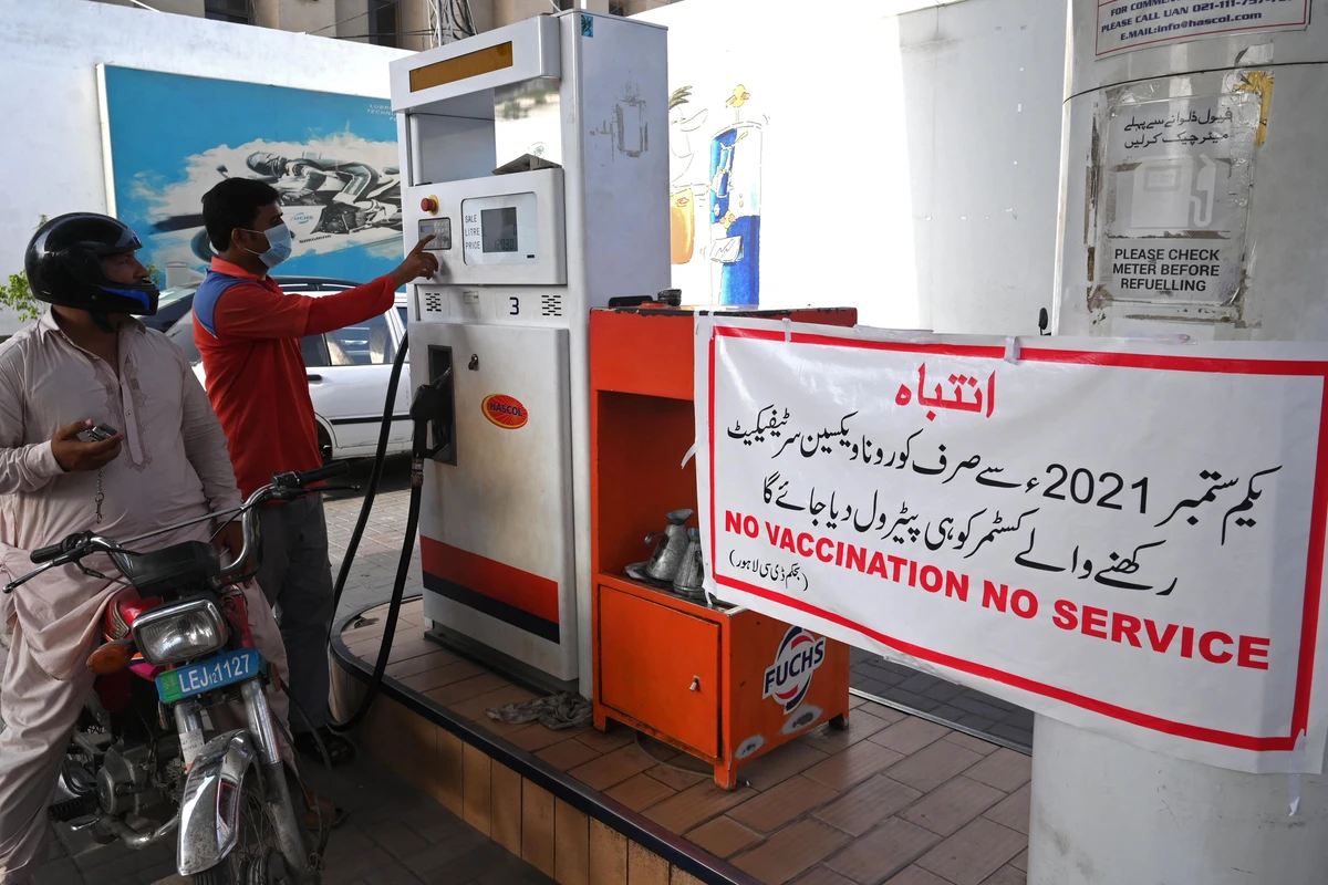 A worker prepares to fill the petrol tank of a motorbike next to a banner warning customers about the guidelines that from September onwards only Covid-19 coronavirus vaccinated customers will be allowed to purchase the fuel in Punjab province, in Lahore on August 27, 2021. (AFP)