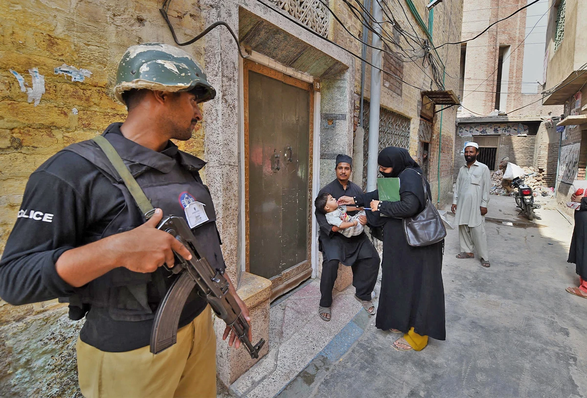 A Pakistani policeman stands guard as a health worker administers polio drops to a child during a polio vaccination campaign in Peshawar, Pakistan, on September 14, 2015. (AFP/File)