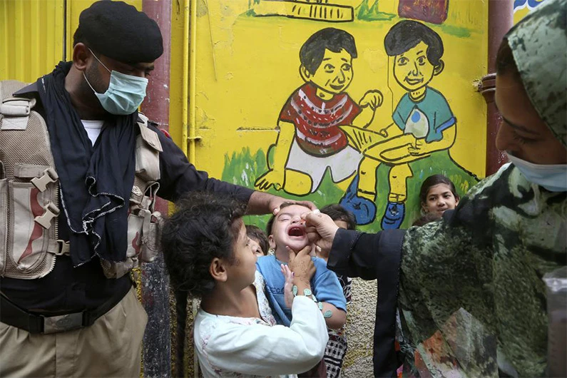 A police officer helps a health worker administer a polio vaccine to a child in Peshawar, Pakistan, Friday, July 30, 2021. (Photo courtesy: AP)