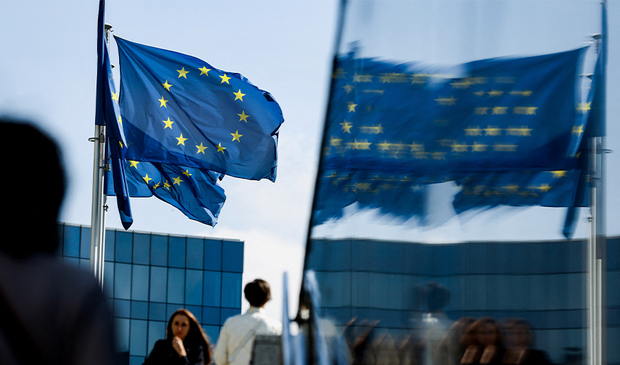 People walk in front of the European Union flag in the area of the EU headquarters in Brussels on September 23, 2021. (AFP)
